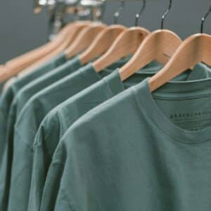 A row of green t-shirts hanging on wooden hangers against a grey background
